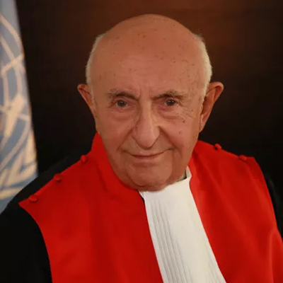 Colour profile pic of Theodor Meron showing the author in red robes before the UN flag.