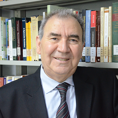 Author profile pic of a smiling author facing the camera in front of a library shelving of books.