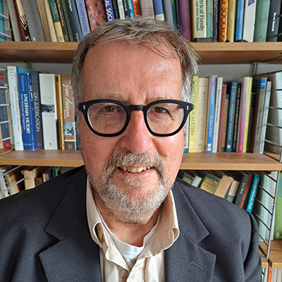 Author profile pic of smiling author in front of a book case